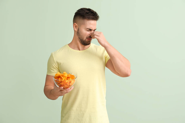 Unzufriedener junger Mann mit Kartoffelchips auf farbigem Hintergrund - Foto, Bild