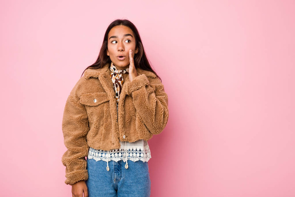 Young mixed race indian woman wearing a short sheepskin coatis saying a secret hot braking news and looking aside - Foto, afbeelding