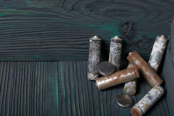 Spent finger-type batteries coated with corrosion. They lie on brushed pine boards painted in black and green. - Fotoğraf, Görsel