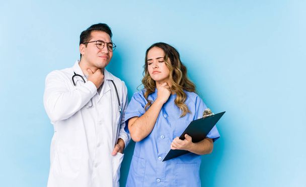 Joven pareja de médicos posando en un fondo azul aislado sufre dolor de garganta debido a un virus o infección
. - Foto, Imagen