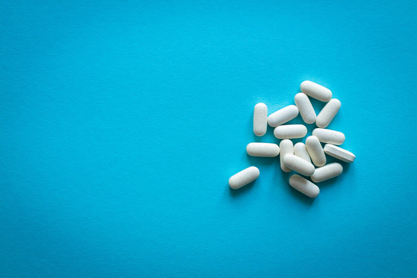 White vitamins on a blue background, scattered drugs. Photo with soft focus, macro shot. - Fotoğraf, Görsel