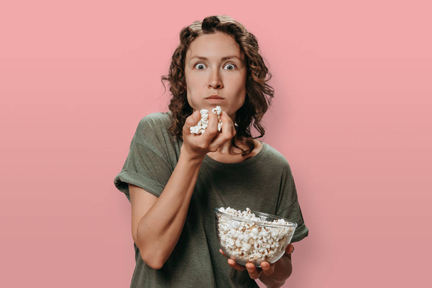 junge Frau mit lockigem Haar, die Popcorn isst, einen Film anschaut oder  - Foto, Bild