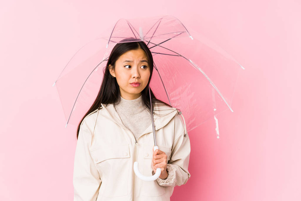 Jovem chinesa segurando um guarda-chuva isolado confuso, se sente duvidoso e inseguro
. - Foto, Imagem