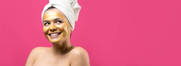 Retrato de belleza de mujer en toalla blanca en la cabeza con máscara nutritiva de oro en la cara. Limpieza de la piel ecológico cosmético spa relajante concepto
. - Foto, Imagen