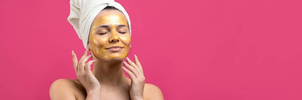 Yüzünde altın besleyici maske olan beyaz havluyla kadın portresi. Cilt temizleme eko organik kozmetik rahatlama konsepti. - Fotoğraf, Görsel