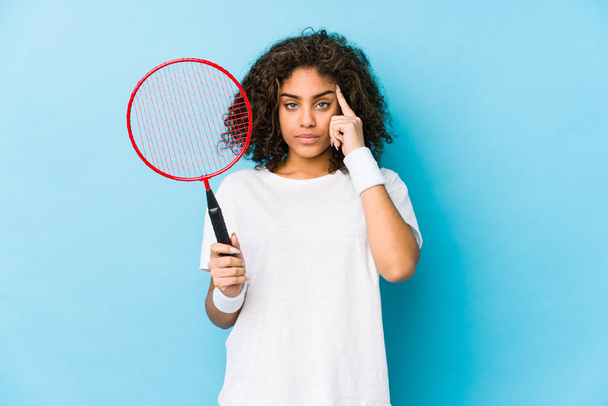 junge afrikanisch-amerikanische Frau spielt Badminton und zeigt mit dem Finger auf die Schläfe, denkt nach, konzentriert sich auf eine Aufgabe. - Foto, Bild