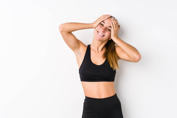 Young caucasian fitness woman posing in a white background laughs joyfully keeping hands on head. Happiness concept. - Photo, image