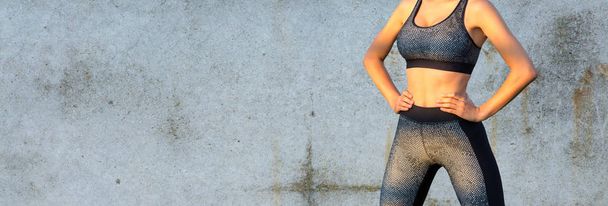 Sportowa szczupła dziewczyna w legginsach i blat stoi pod betonową ścianą i wykonuje zestaw ćwiczeń. - Zdjęcie, obraz