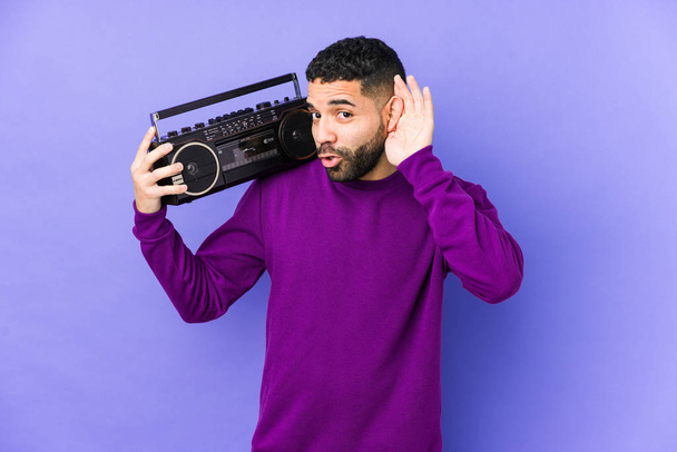 młody arabski człowiek trzymając kasetę radiową odizolowany młody arabczyk słuchający muzyki próbujący słuchać plotek. - Zdjęcie, obraz