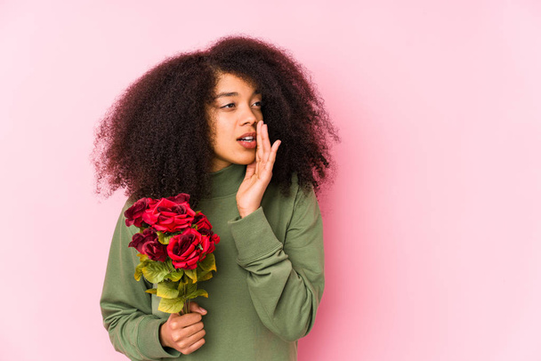 Молодая афро-женщина, держащая в руках розы, молодая афро-женщина, держащая в руках розовый розезис, рассказывая секретные горячие новости о торможении и глядя в сторону
 - Фото, изображение