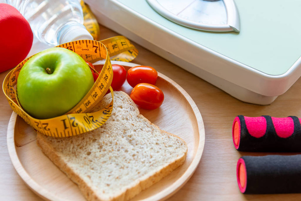 Terveellinen elämäntapa naisille ruokavalio paino mittakaavassa käsipainot urheiluvälineet, lenkkarit, mittanauha, hedelmiä terveellisiä vihreitä omenoita ja pullo vettä puinen. Terveellinen käsite
. - Valokuva, kuva