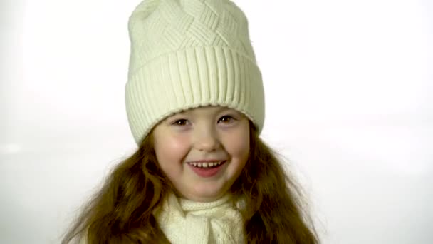 Little girl in a white knitted hat. Beautiful little girl in cap and scarf isolated on white. - Imágenes, Vídeo