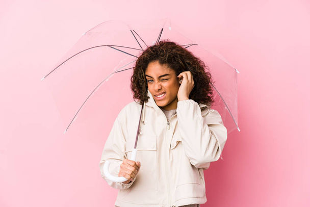 Young african american woman holding a umbrella covering ears with hands. - 写真・画像