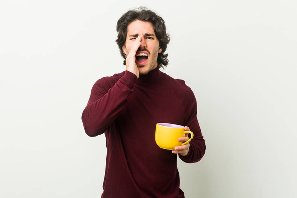 Молодий білий чоловік тримає чашку кави, що кричить, збуджений на передній план
. - Фото, зображення