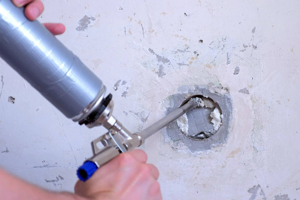 Man fills hole in wall of concrete slab mounting foam making repairs at home. - Foto, Bild