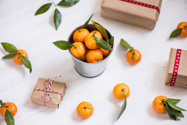 Christmas decoration of mandarin in an iron small bucket, Christmas tree, gifts  on the white wooden boards background - Φωτογραφία, εικόνα