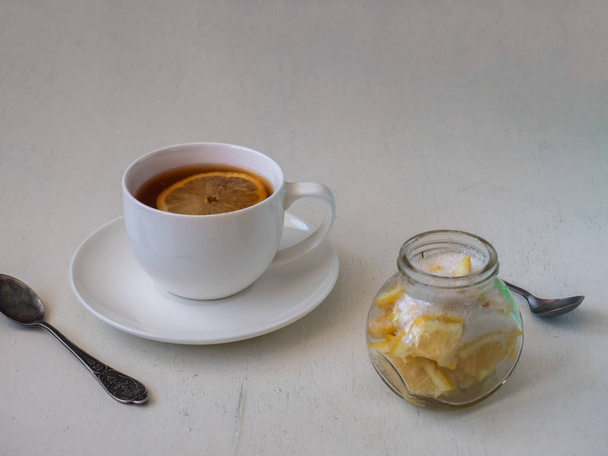 Egy csésze tea citrommal egy könnyű asztalon, és egy konzerv citrommal. - Fotó, kép
