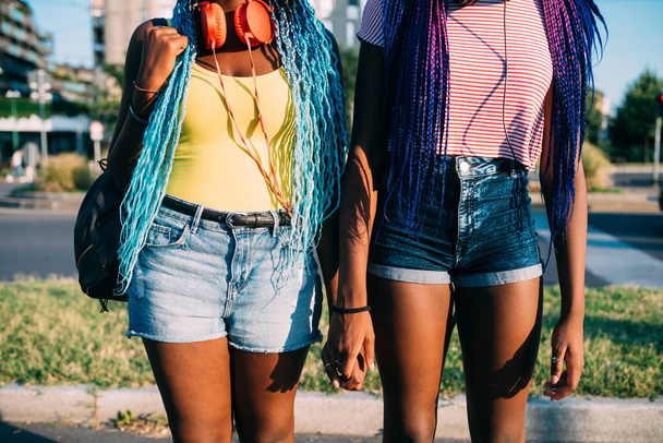 Im Mittelteil zwei junge schwarze Frauen im Freien, die Händchen halten  - Foto, Bild