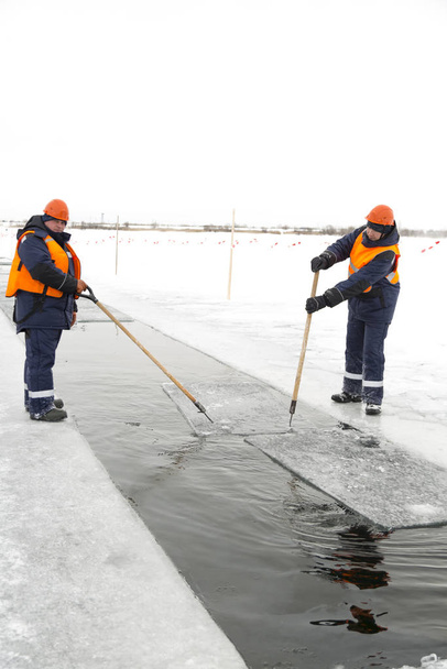 Workers rafting ice blocks along a channel cut out by a frozen lake - 写真・画像