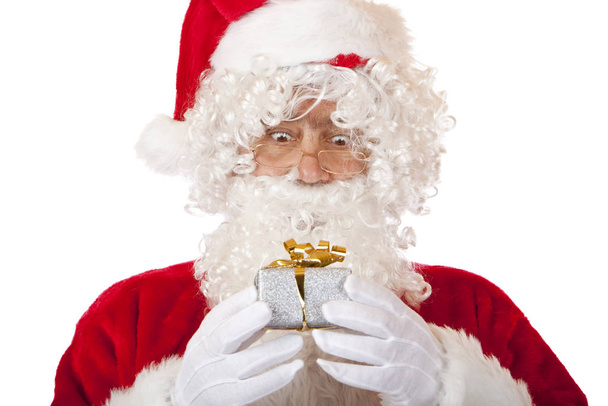Old Santa Claus holding Christmas gift in hands and looks surpri - Фото, изображение