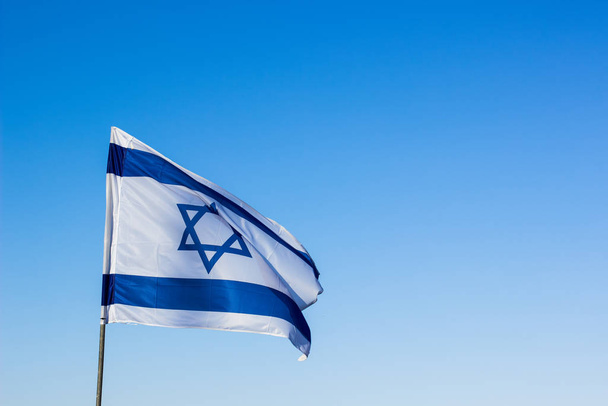 Israeli flag with star of David national symbol fluttering on empty blue sky background copy space for your text here - Foto, imagen