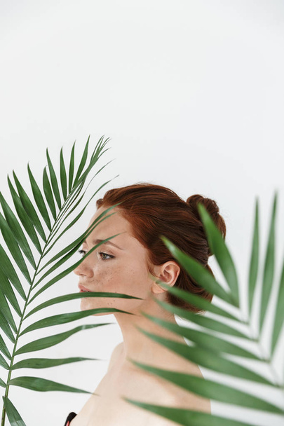 Young redhead woman posing isolated over white wall background with leaf green flowers. - Фото, зображення
