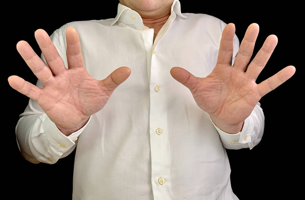 Mężczyzna trzyma dwie ręce przed sobą. Mężczyzna w białej koszuli pokazuje gest dłoni, na czarnym tle. Koncepcja: strach, odrzucenie. - Zdjęcie, obraz