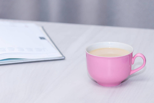 Roze kop koffie, open notitieboekje op houten bureau tafel. Freelancer of bloger, copywriter concept. - Foto, afbeelding