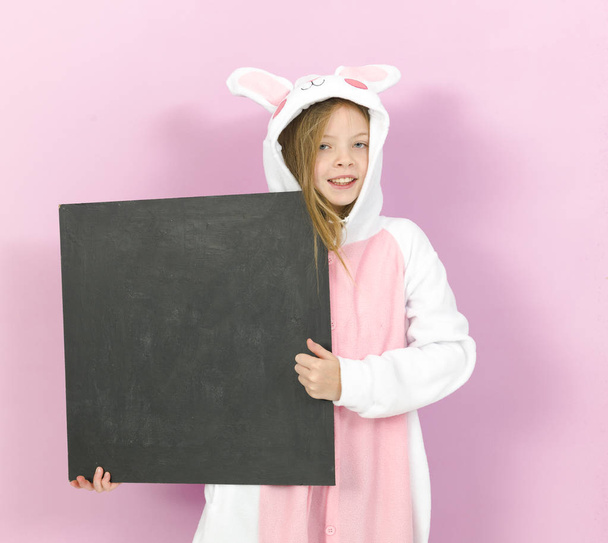 happy pretty blonde girl in cozy rabbit costume with empty blackboard posing in studio  - Foto, imagen