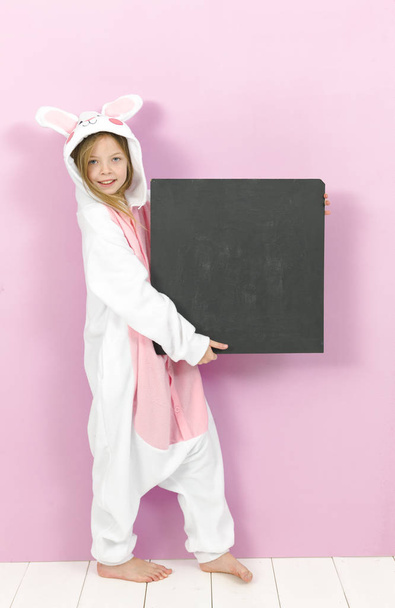 happy pretty blonde girl in cozy rabbit costume with empty blackboard posing in studio  - Fotografie, Obrázek