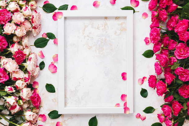 Various brightly colored pink and red roses directed at each other on rustic white and gold surface and empty white wooden frame.  Top view, blank space - Фото, зображення