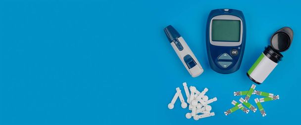 Glucometer. A device for measuring blood sugar levels. Test strips, pills on a blue background. - Foto, imagen