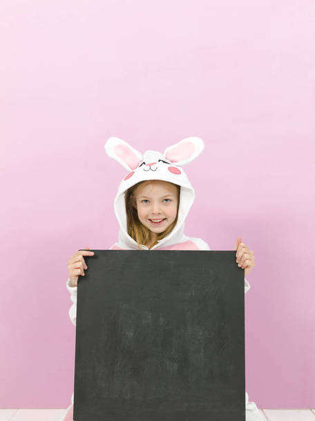 happy pretty blonde girl in cozy rabbit costume with empty blackboard posing in studio  - Valokuva, kuva