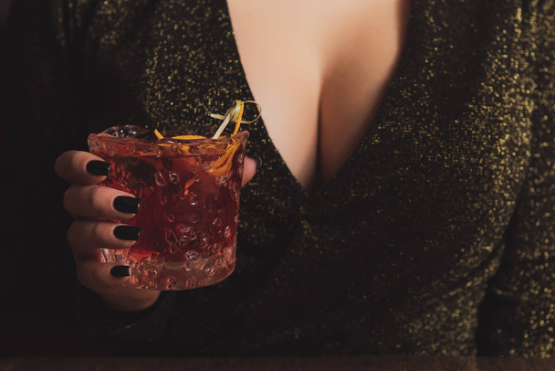 Fille en robe de soirée avec un gros sein tient un cocktail d'alcool dans une main. Femme chaude à la fête. Tentation dans un bar avec décolleté sexy. Concept de consommation photo
. - Photo, image