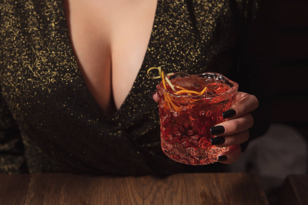Girl in evening dress with big breast holds an alcohol cocktail in a hand. Hot woman at the party. Temptation in a bar with sexy neckline. Consummation concept photo. - Fotoğraf, Görsel