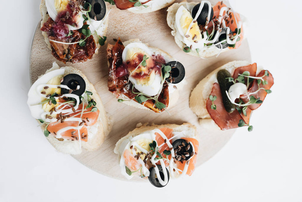 Delicious fresh bruschettas with eggs, salmon, olives and meat , traditional Italian cuisine, ingredients on white  table - Fotoğraf, Görsel