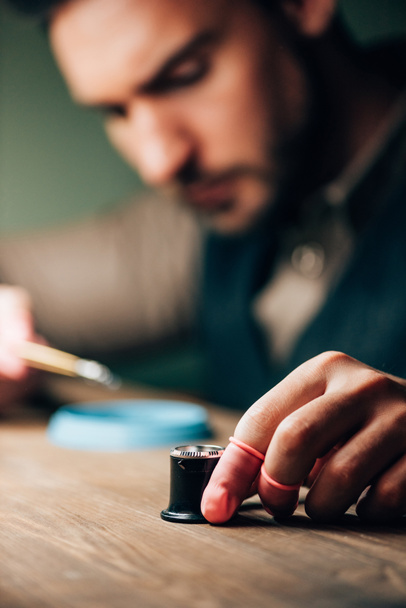 Выборочный фокус часовщика, держащего в руках лупу для очков во время работы за столом
 - Фото, изображение