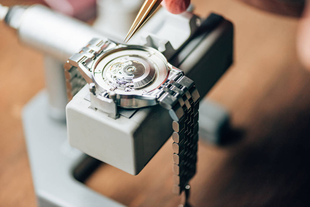 Ausgeschnittene Ansicht eines Uhrmachers, der mit Pinzette und Armbanduhr am Werkhalter arbeitet  - Foto, Bild
