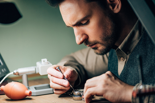 Side view of watchmaker working with screwdriver and wristwatch by equipment on table - Fotografie, Obrázek