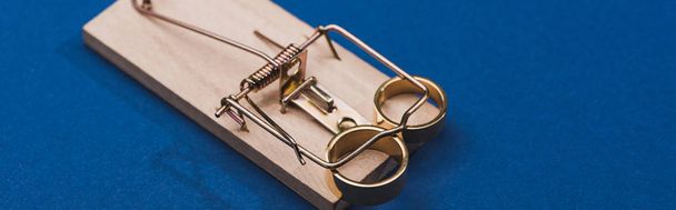 Panoramic shot of golden jewellery rings in wooden mouse trap on blue background - Foto, Imagem