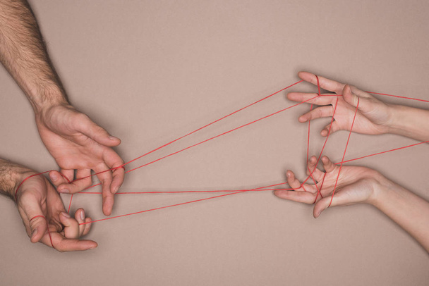 Top view of man and woman holding red string on beige background - Foto, Bild