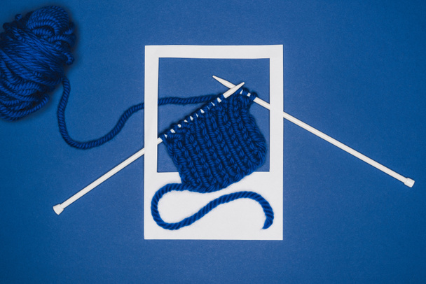 Top view of knitting needles with yarn in white photo frame on blue background - Zdjęcie, obraz