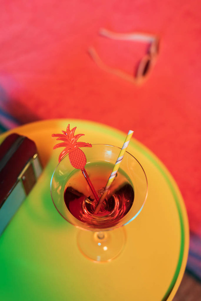 Gele tafel met cocktaildrankje en draagbare radio naast de zonnebank - Foto, afbeelding