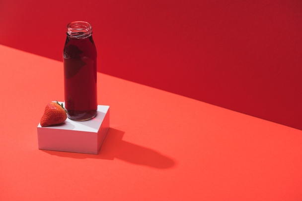 fresh berry juice in glass bottle near ripe strawberry on cube on red background - Fotoğraf, Görsel