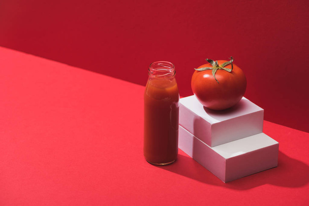 zumo de verduras frescas en botella de vidrio cerca de tomate maduro en pie sobre fondo rojo
 - Foto, Imagen