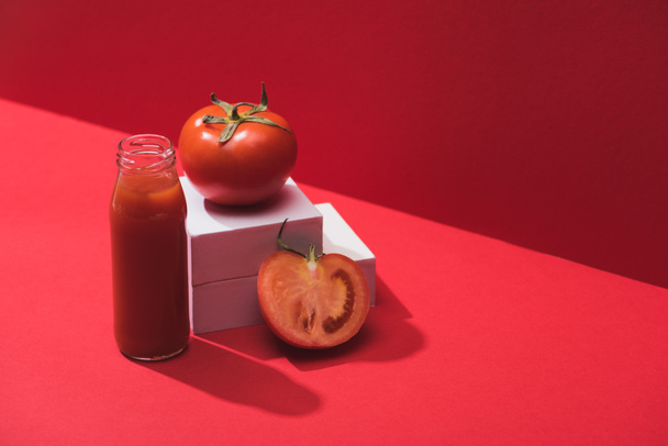 jugo de verduras frescas en botella de vidrio cerca de tomates maduros en cubos sobre fondo rojo
 - Foto, Imagen
