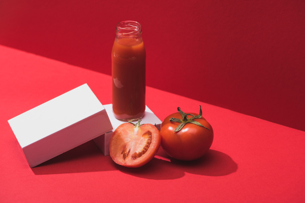 fresh vegetable juice in glass bottle and ripe tomatoes on cubes on red background - 写真・画像