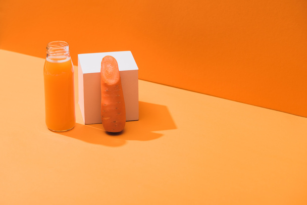 zumo fresco en botella de vidrio cerca de zanahoria madura y cubo sobre fondo naranja
 - Foto, imagen