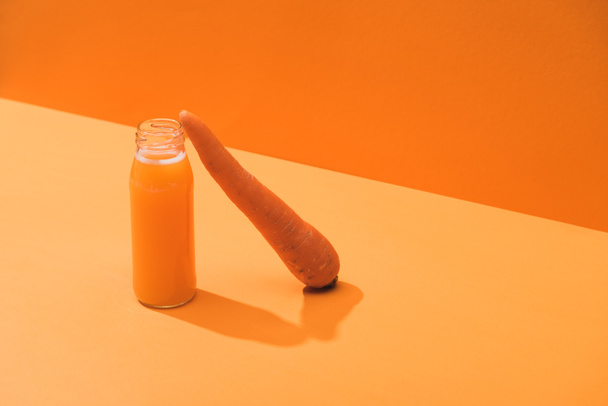 fresh juice in glass bottle near ripe carrot on orange background - Foto, Bild