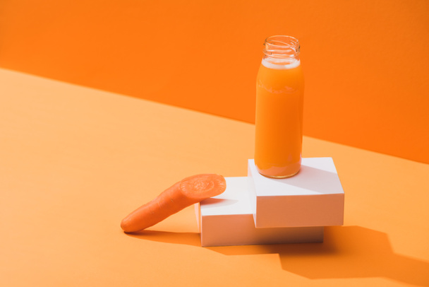 fresh juice in glass bottle near ripe carrot on cubes on orange background - Fotó, kép